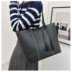 Macro detail of black tote bag showing white contrast stitching and tassel pendant decor