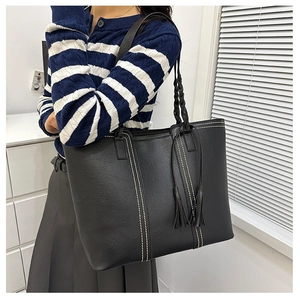 Detail of black leather tote bag featuring contrast white stitching and tassel accents