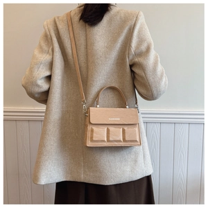 Detail of light brown crossbody bag featuring 3D embossed squares and top handle