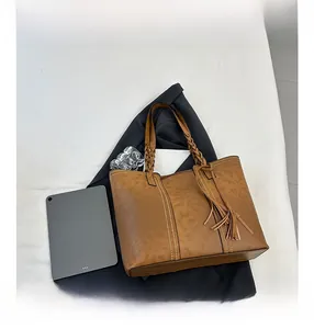 Close-up of brown tote bag showing woven handles, tassels and contrast stitching detail