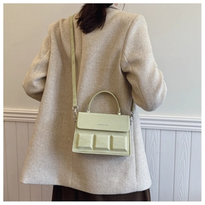 Detail of light green box bag with embossed squares and shoulder strap on model