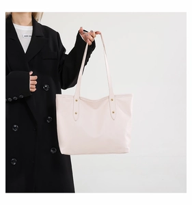 Detailed view of the large beige tote bag featuring metallic rivets and slim handles