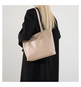 Close-up of a beige large tote bag with leather texture worn over a black blazer