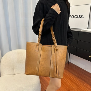 Caramel large tote bag with woven handle and fringe tassel shown in use for commute