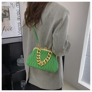 Green pleated shell bag with gold chain strap worn with a gray suit in modern setting