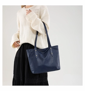 Detail of dark blue crocodile embossed tote bag with gold rivets on shoulder strap
