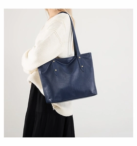 Detail of dark blue tote bag featuring crocodile embossed texture and gold metal buckles