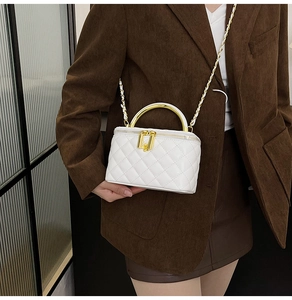 Gros plan sur le sac matelassé blanc avec poignée dorée porté sur un blazer marron