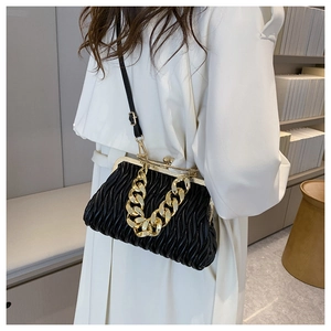 Detail of black pleated shell bag with gold chain strap worn as a crossbody bag