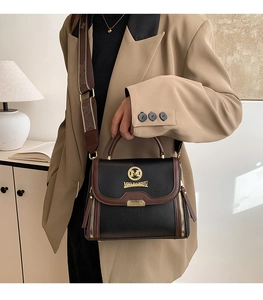 Vue détaillée du sac à main en cuir noir avec bandoulière large à motifs et logo doré