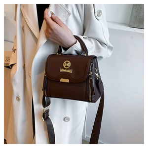 Détail du sac à main marron avec texture litchi et large bandoulière porté par le mannequin