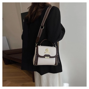 Détail du sac en cuir crème avec bordure marron, logo doré et large bandoulière