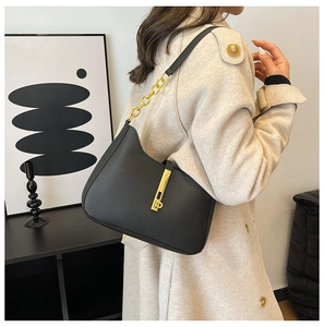 Close-up of black leather shoulder bag with gold metal hardware on beige coat