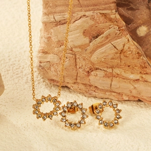 Goldenes Zirkonia Schmuckset mit Halskette und Ohrringen auf weißem Steinuntergrund