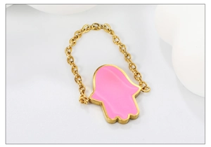 Macro shot of gold link chain ring featuring a pink enamel Hamsa hand charm detail