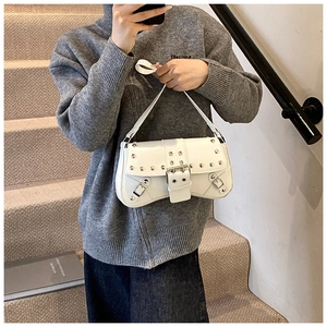Détail d'un sac baguette en cuir blanc avec clous argentés et sangles à boucles