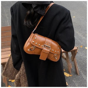 Détail du sac en cuir marron avec clous argentés et boucle métallique sur fond d'automne