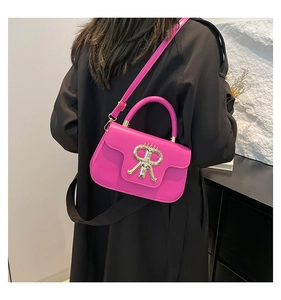 Detailed view of the rose pink crossbody bag with gold logo on a black wool coat