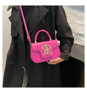 Side view of a bright rose pink crossbody bag with golden RR buckle on a black trench coat