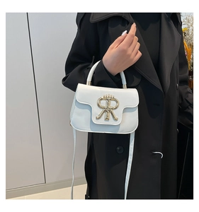 Detail of white leather handbag with elegant gold crown buckle on black coat background