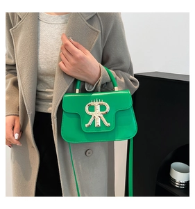 Detail of green leather handbag with gold R-shaped lock on a grey wool coat background