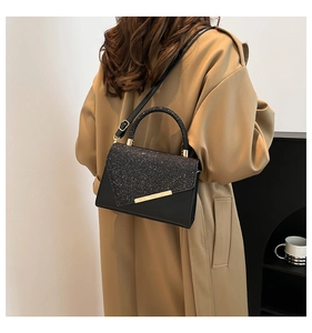 Detail view of black faux leather handbag featuring silver glitter flap and gold metal trim