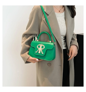 Detail of vibrant green leather handbag with gold R buckle on a grey coat background