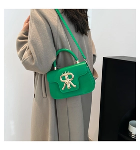 Detail of bright green leather handbag with gold R buckle on model wearing beige coat