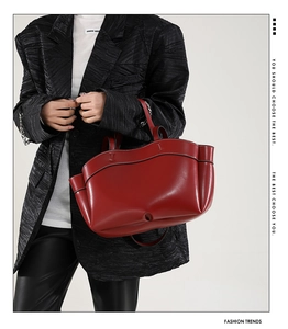 Dettaglio della borsa tote in pelle rossa con bordi ondulati tenuta da modella in nero