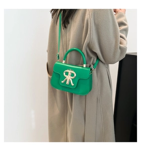 Detail of vibrant green leather handbag featuring golden metal logo and stitching