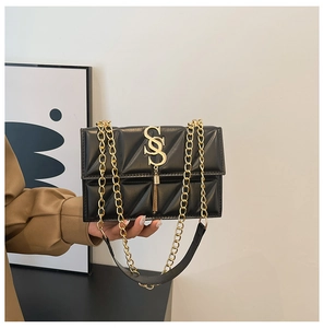Détail d'un sac bandoulière noir matelassé avec chaîne dorée et pendentif à glands