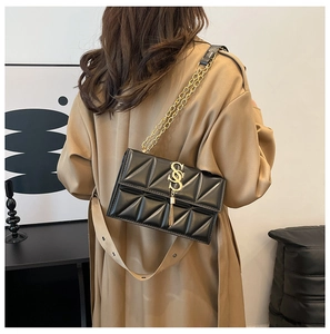 Detail view of a black quilted crossbody bag with gold SS logo and tassel on a model