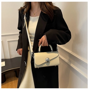 Detail of minimalist beige box bag featuring a polished silver ball clasp and leather texture