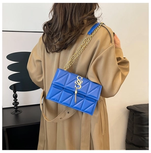 Blue quilted faux leather crossbody bag with gold chain strap on model in home setting