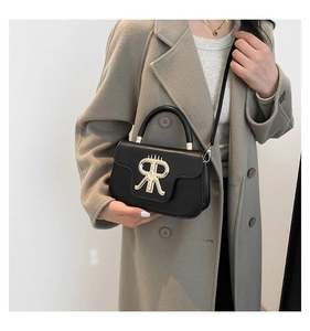 Close-up of structured black handbag with gold RR hardware on a neutral coat