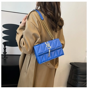 Détail d'un sac bandoulière matelassé bleu électrique avec chaîne dorée sur un trench