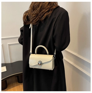 Close-up of a minimalist cream box bag with silver round buckle and adjustable strap