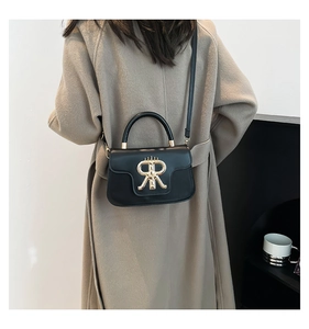 Detail of a chic black leather handbag with a gold metal RR logo on a beige coat outfit