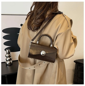 Detail of a dark brown patent leather box bag with a silver sphere lock and wide strap