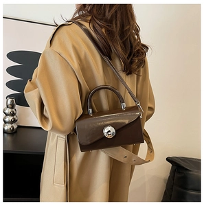 Detail of dark brown glossy leather box bag featuring a silver spherical metal buckle