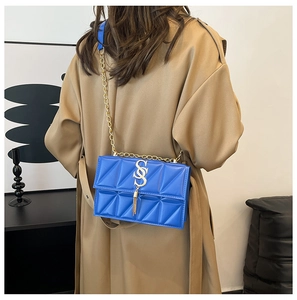 Royal blue quilted shoulder bag with gold chain strap shown on a khaki trench coat