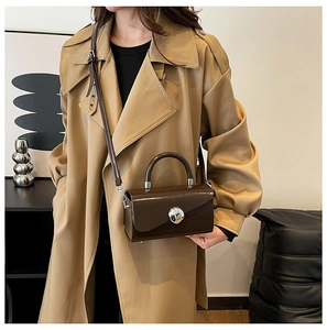 Detail of dark brown glossy box bag with silver spherical lock on trench coat background