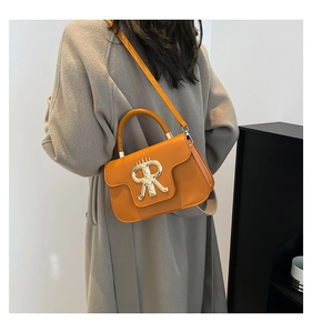 Detail of a bright orange square handbag with golden metal RR logo and smooth texture