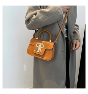 Detail of orange square handbag showing fine grain leather texture and golden metal logo