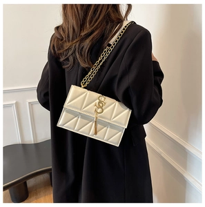 Close-up of white quilted crossbody bag with gold S-shaped buckle and tassel detail
