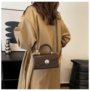 Detail of dark brown glossy leather handbag with circular silver metal buckle on model