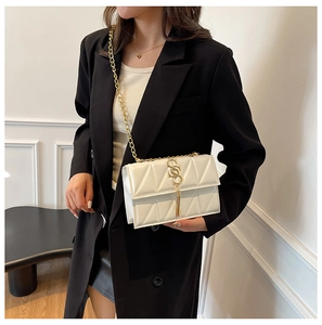 Close-up of white quilted crossbody bag with gold S-logo and metal tassel detail