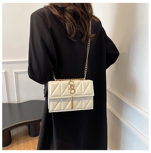 Detail of a chic cream quilted crossbody bag with gold chain strap and tassel on a model