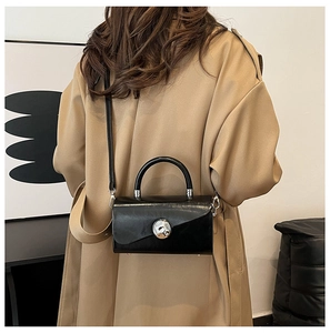 Detail of black leather square handbag with silver round buckle shown on a model