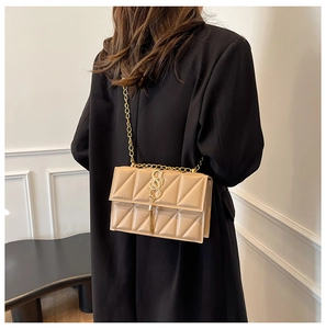 Detail of light beige quilted chain bag with gold S logo and fringe on a black blazer